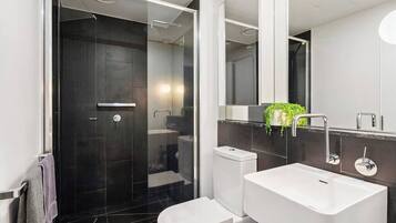 A modern bathroom with a glass-enclosed shower, a white toilet, and a large sink with a mirror above.
