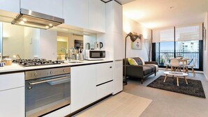 A modern kitchen with built-in appliances, a dining area with a table and chairs, and a sofa. - Nora - Superb designer style *WIFI Parking (Melbourne)