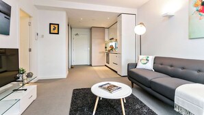 A modern living room with a sofa, a coffee table, a TV, and a kitchen in the background. - Nora - Superb designer style *WIFI Parking (Melbourne)