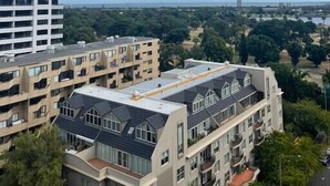 A high-rise building with multiple balconies, a flat-roofed building with large windows, and a park with trees and a lake in the background. - Nora - Superb designer style *WIFI Parking (Melbourne)