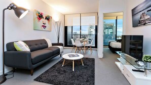 A modern living room with a sofa, coffee table, TV, and dining area with chairs. - Nora - Superb designer style *WIFI Parking (Melbourne)