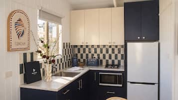 A compact kitchen with a sink, stove, and refrigerator, featuring a checkered backsplash and dark cabinetry.