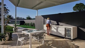 An outdoor kitchen area with a built-in grill, a dining table with chairs, and a covered patio. - Yerriyong 2 - Family Cabin Sleeps 5 Mollymook (Mollymook)