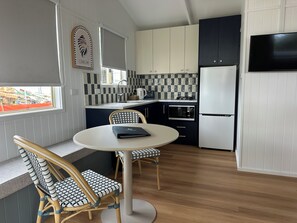 A compact kitchen with a dining area, featuring a round table, two chairs, a built-in oven, a microwave, and a refrigerator. - Yerriyong 2 - Family Cabin Sleeps 6 Mollymook (Mollymook)
