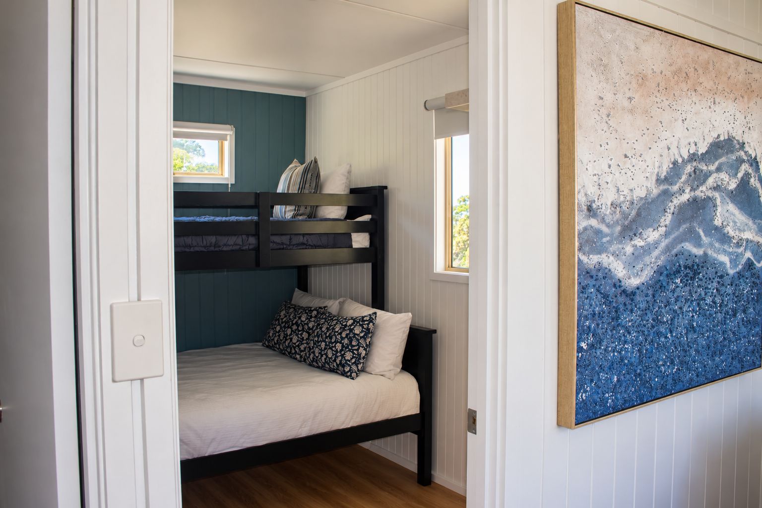 A bedroom with a bunk bed, a single bed, a window, and a painting on the wall.