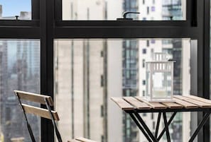 A view through a window with a table and a chair, a candle holder, and a building in the background. - Riley - Resort Living * Gym Sauna Pool Wi-Fi (Southbank)