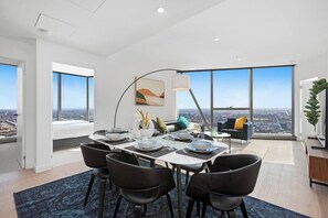 Ein moderner Essbereich mit hohem Tisch, gedeckt für sechs Personen, großen Fenstern mit Blick auf die Stadt und einer gemütlichen Sitzecke mit Sofa und Sesseln.