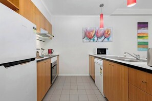 Eine kompakte Küche mit weißen Schränken, einer Mikrowelle, einem Spülbecken und einem Geschirrspüler. An der Wand hängt ein Blumenbild.