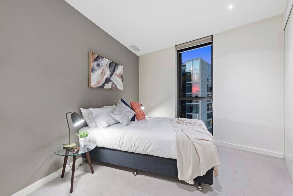 A modern bedroom with a bed, a glass table, a plant, and a city view.