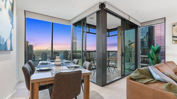 Ein modernes Wohnzimmer mit Essbereich, große Glasüren führen zu einem Balkon mit Blick auf die Stadt.