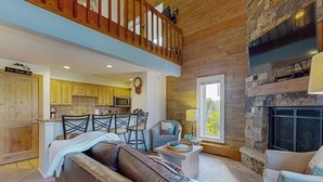 Ein geräumiges Wohnzimmer mit einer Ledersofa, einem Essbereich mit Stühlen, einer Küche mit Holzschränken und einem Kamin aus Stein.