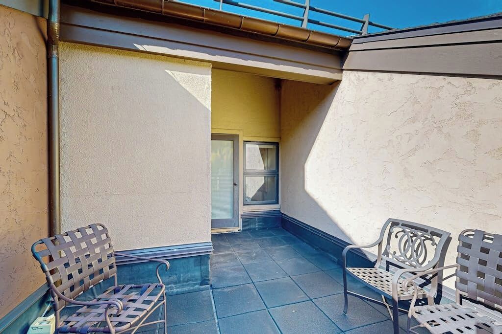 Een balkon met twee rieten stoelen, een raam en een deur.