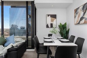 Ein modernes Esszimmer mit Esstisch für vier Personen, einer Couch mit Kissen, einem großen Fenster mit Stadtblick und einem Gemälde an der Wand.
