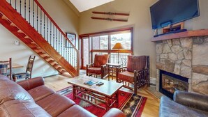 A spacious living room with a wooden staircase, a stone fireplace, and a large window. - Ski-in/ski-out condo w/ grill, fast WiFi, fireplace, shared pool/hot tub/laundry (Vail)