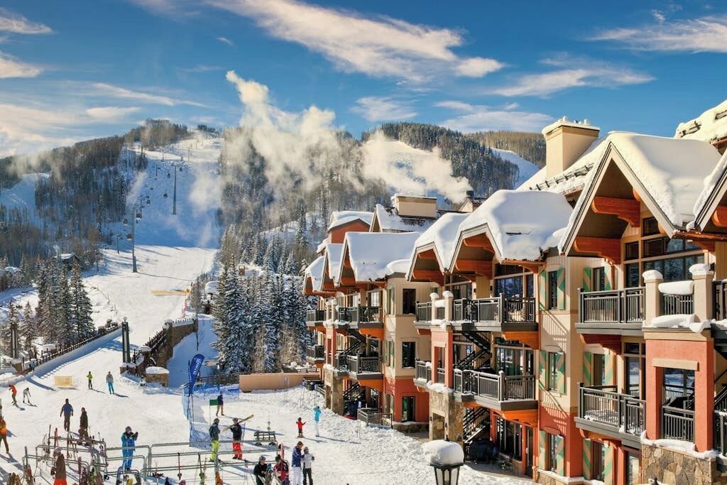 A ski resort with multi-story buildings, a ski slope, and a snowy mountain backdrop.