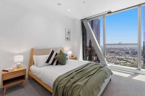 A modern hotel room with a large bed, a nightstand, a lamp, and a view of a cityscape through a large window. - Executive stunner in West Side Place with Parking (Melbourne)