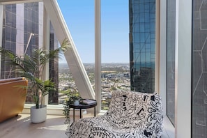 A modern room with a large window, a potted plant, a patterned sofa, and a small table. - Executive stunner in West Side Place with Parking (Melbourne)