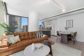 A modern living room with a brown leather sofa, a round coffee table, and a dining area with a white table and brown chairs. - Executive stunner in West Side Place with Parking (Melbourne)