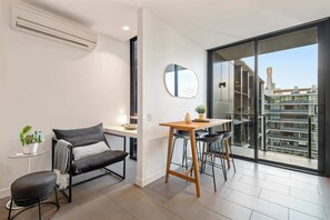 A modern living space with a sofa, a small table, a chair, and a large window offering a city view. - Edy - Southbank Stunner with WIFI Parking (South Melbourne)