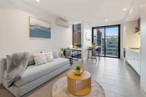 A modern living room with a grey sofa, a round coffee table, and a dining area with a small table and chairs. - Edy - Southbank Stunner with WIFI Parking (South Melbourne)