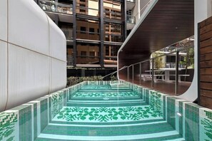 A modern indoor pool with a geometric tile design, surrounded by high-rise buildings and a curved wooden structure. - Edy - Southbank Stunner with WIFI Parking (South Melbourne)