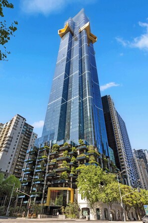 A tall, modern skyscraper with a unique top design, surrounded by other high-rise buildings. - Executive living in Melbourne's best location. (Southbank)