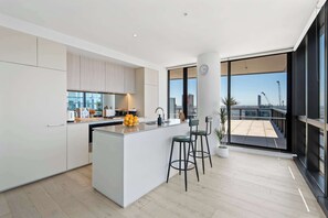 Eine moderne Küche mit einer zentralen Kochinsel, Barhocker und Blick auf eine Baustelle durch große Fenster.