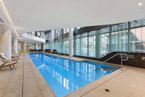 Ein Hallenbad mit klarem Wasser, einem Sprungturm und Liegestühlen.