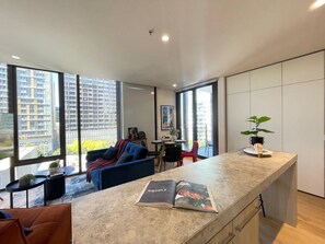 A modern kitchen with large windows, a dining area, and a living space with a sofa and chairs. - Southbank stunner with parking views gym and pool! (South Melbourne)