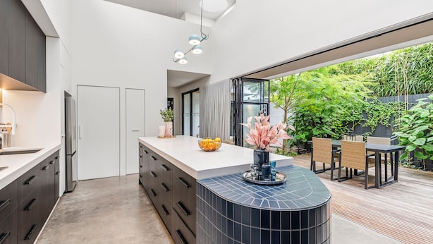 A modern kitchen with a central island, a dining area with outdoor seating, and a view of greenery. - Architectural Masterclass in UberHip Northcote. (Northcote)