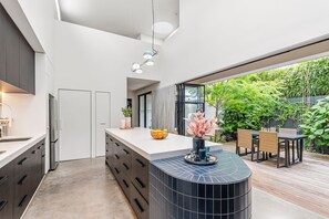 A modern kitchen with a central island, a dining area with outdoor seating, and a view of greenery.