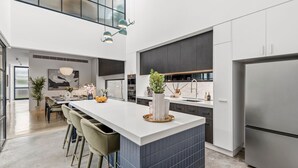 A modern kitchen with a central island, bar stools, and a large refrigerator. - Architectural Masterclass in UberHip Northcote. (Northcote)