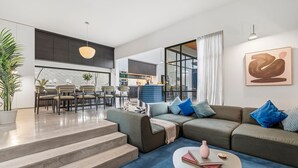 A modern living room with a sofa, coffee table, and a dining area with chairs and a kitchen in the background. - Architectural Masterclass in UberHip Northcote. (Northcote)