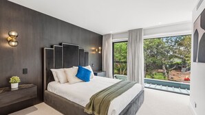 A modern bedroom with a large bed, a nightstand, a wall-mounted light fixture, and a view of the outdoors. - Architectural Masterclass in UberHip Northcote. (Northcote)