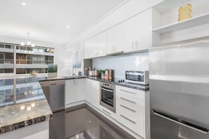 A modern kitchen with white cabinetry, a stainless steel refrigerator, a built-in oven, and a granite countertop. - Stunning Large 2BD Parkside Apartment with Parking (Melbourne)