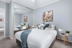 A bedroom with a bed, bedside tables, a mirror, and wall art. - Stunning Large 2BD Parkside Apartment with Parking (Melbourne)