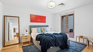 Una camera da letto con un letto, un comodino, una lampada, uno specchio, un quadro astratto rosso e una porta scorrevole in vetro.
