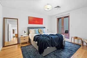 Ein Schlafzimmer mit Bett, Nachttisch, Lampe, Spiegel, einem roten abstrakten Gemälde und einer Schiebeglastür.