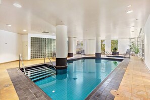 Ein Hallenbad mit Fliesenboden, einer Poolleiter und einer gefliesten Wand im Hintergrund.