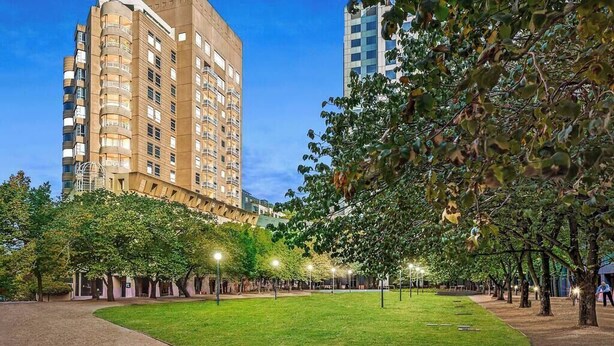 Un parco con prato, alberi e un edificio a più piani con balconi.
