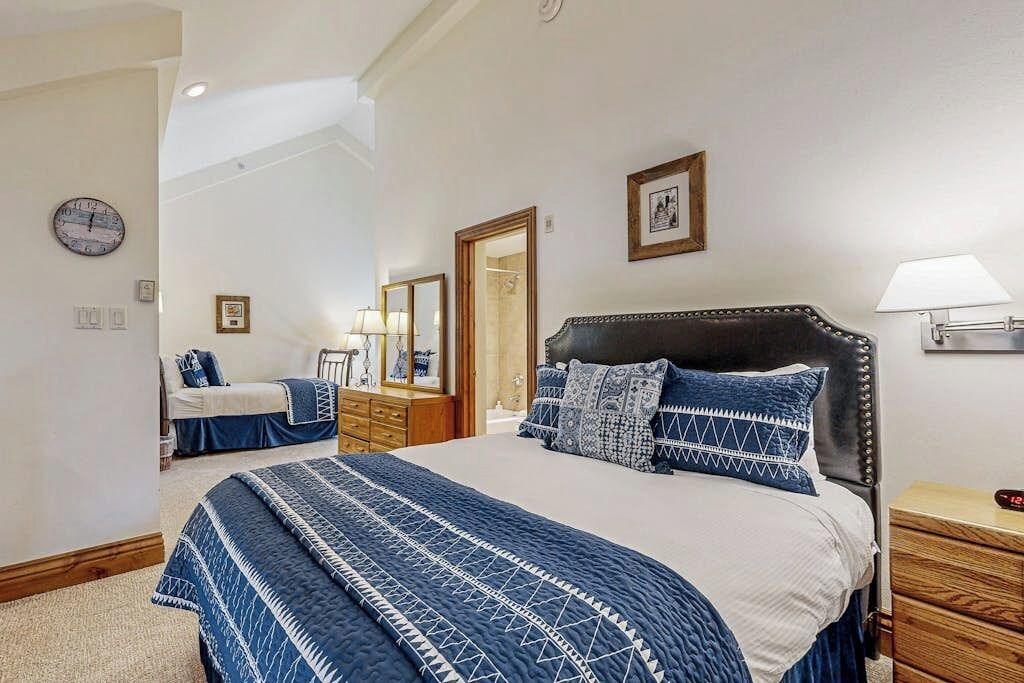 A bedroom with a large bed, a dresser, a nightstand, a mirror, and a clock on the wall.