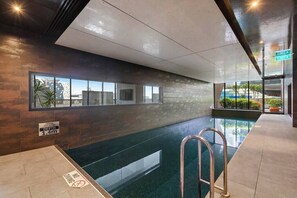 Ein Hallenbad mit Tiefenhinweisschildern, Ausgängen und Blick ins Freie.