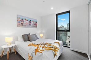 Ein Hotelzimmer mit einem großen Bett, einem Wandbild, einem Fenster mit Blick auf die Stadt und einem kleinen Tisch mit einer Lampe.