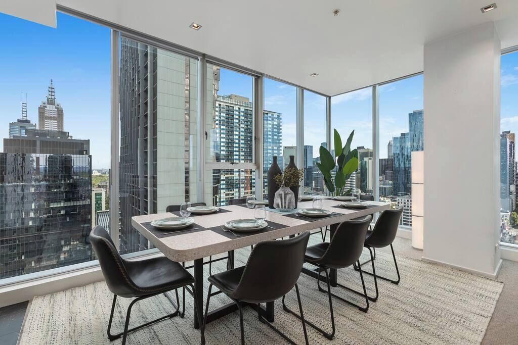 Une salle à manger moderne avec une grande table, des chaises noires et une vue sur la ville.