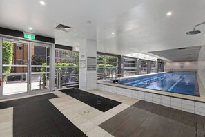Ein Schwimmbeckenbereich mit Glastüren, einer schwarzen Matte und gefliestem Boden.