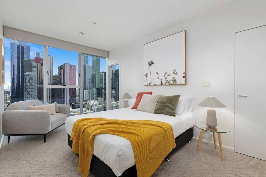 Una habitación de hotel moderna con una cama grande, un sofá, vistas a la ciudad y una obra de arte enmarcada en la pared.