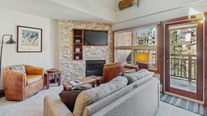 Ein Wohnzimmer mit Steinwand, Flachbildfernseher, Ledersofas und einem Balkon mit Blick.