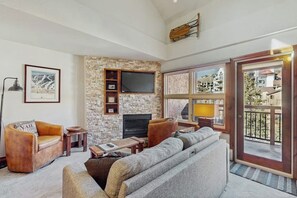 Ein Wohnzimmer mit Steinwand, Flachbildfernseher, Ledersofas und einem Balkon mit Blick.