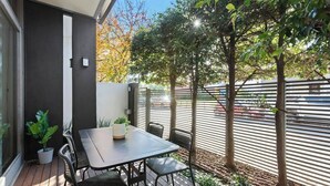 Eine Terrasse mit Tisch und Stühlen, umgeben von Blumentöpfen und Bäumen.