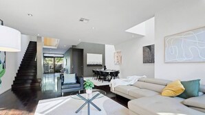 Ein modernes Wohnzimmer mit Treppe, Essbereich und einer Couch mit Kissen.